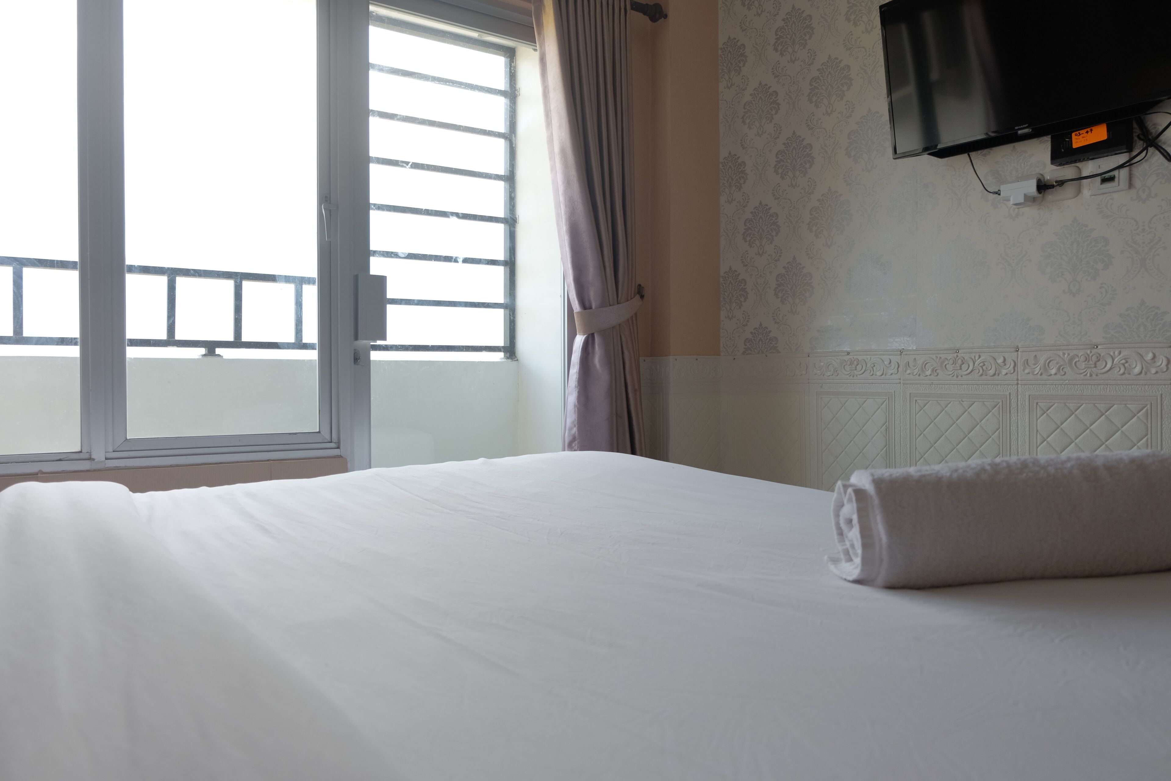 Una habitación de hotel con una cama grande, un televisor montado en la pared y un ventanal con cortinas.