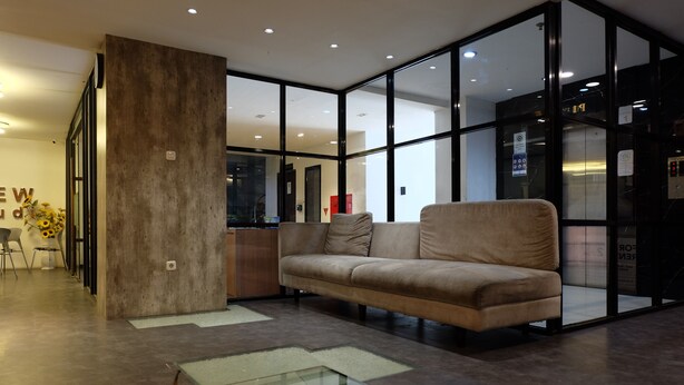 Un hall d’entrée moderne avec une cloison en verre, un canapé beige et une table basse en verre.