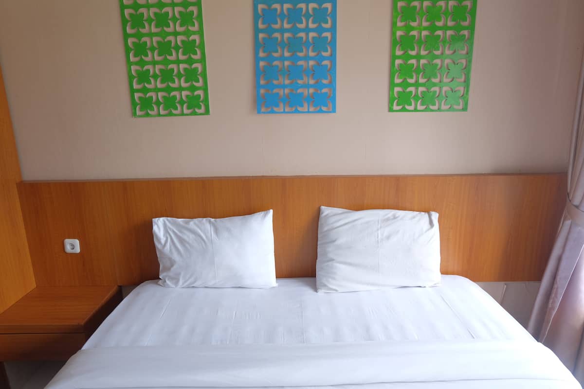A hotel room with a wooden headboard, two white pillows, and a bed with white linens.