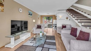 A modern living room with a flat-screen TV, a glass coffee table, a sofa, and a staircase. - Hydra 8 (Merimbula)