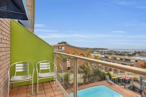 Un balcó amb dues cadires metàl·liques, una piscina i vista a una vila costanera.