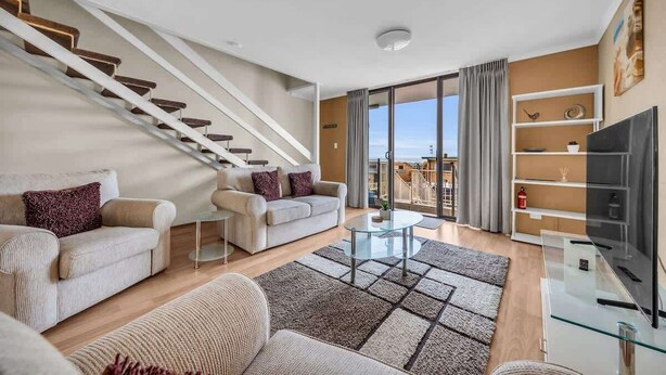 A modern living room with a staircase, a flat-screen TV, and a balcony with a view. - Hydra 8 (Merimbula)