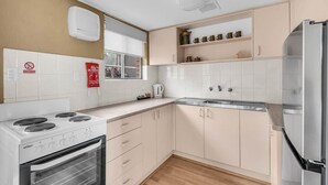 A compact kitchen with a stove, oven, and refrigerator, white cabinets, and a window. - Hydra 8 (Merimbula)