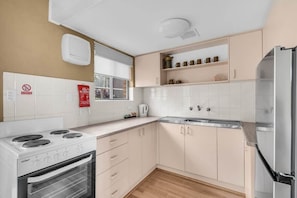 A compact kitchen with a stove, oven, and refrigerator, white cabinets, and a window.