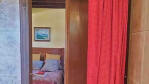 A narrow hallway with a wooden door leading to a bedroom. A red checkered curtain partially covers the door. - THE OLD WOMAN'S HOUSE (Carancos)