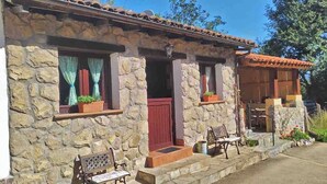 A stone building with a red door, windows with curtains, and a patio area with a bench. - THE OLD WOMAN'S HOUSE (Carancos)