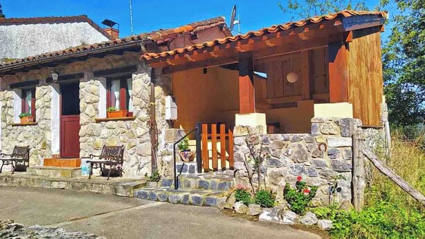 A stone house with a wooden porch, a red door, and a small garden area. - THE OLD WOMAN'S HOUSE (Carancos)
