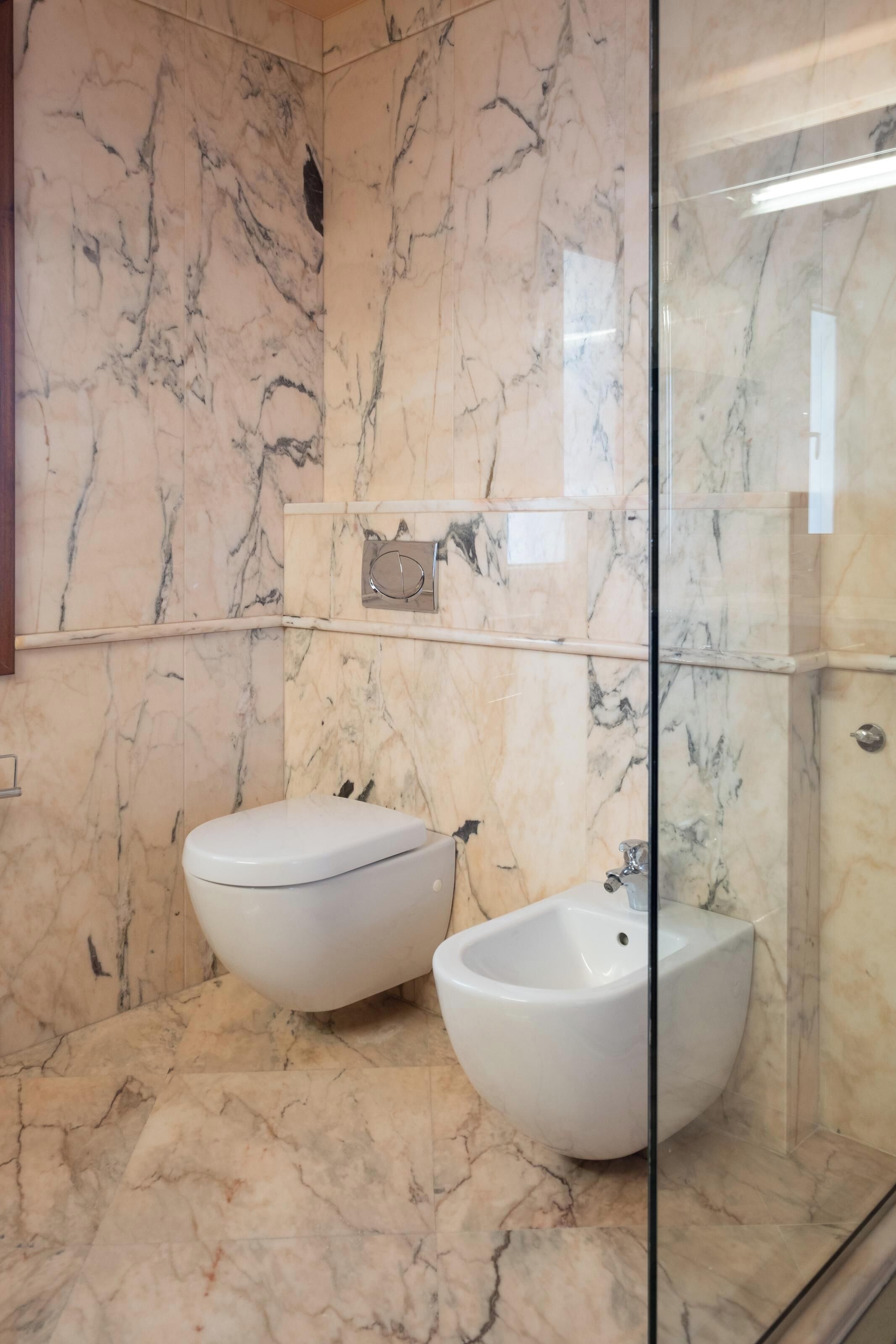 A bathroom with marble walls and a glass shower enclosure.