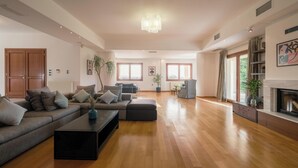 Un salon spacieux avec un grand canapé d’angle, une table basse et une cheminée. De grandes fenêtres laissent entrer la lumière naturelle et offrent une vue sur l’extérieur.