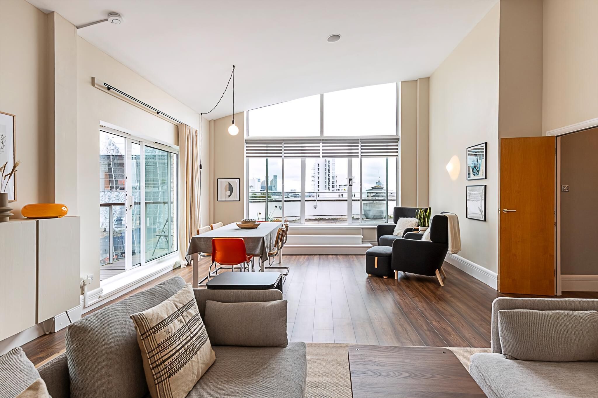 A modern living room with a dining area, large windows, and a view of the city.