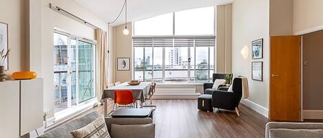 A modern living room with a dining area, large windows, and a view of the city.