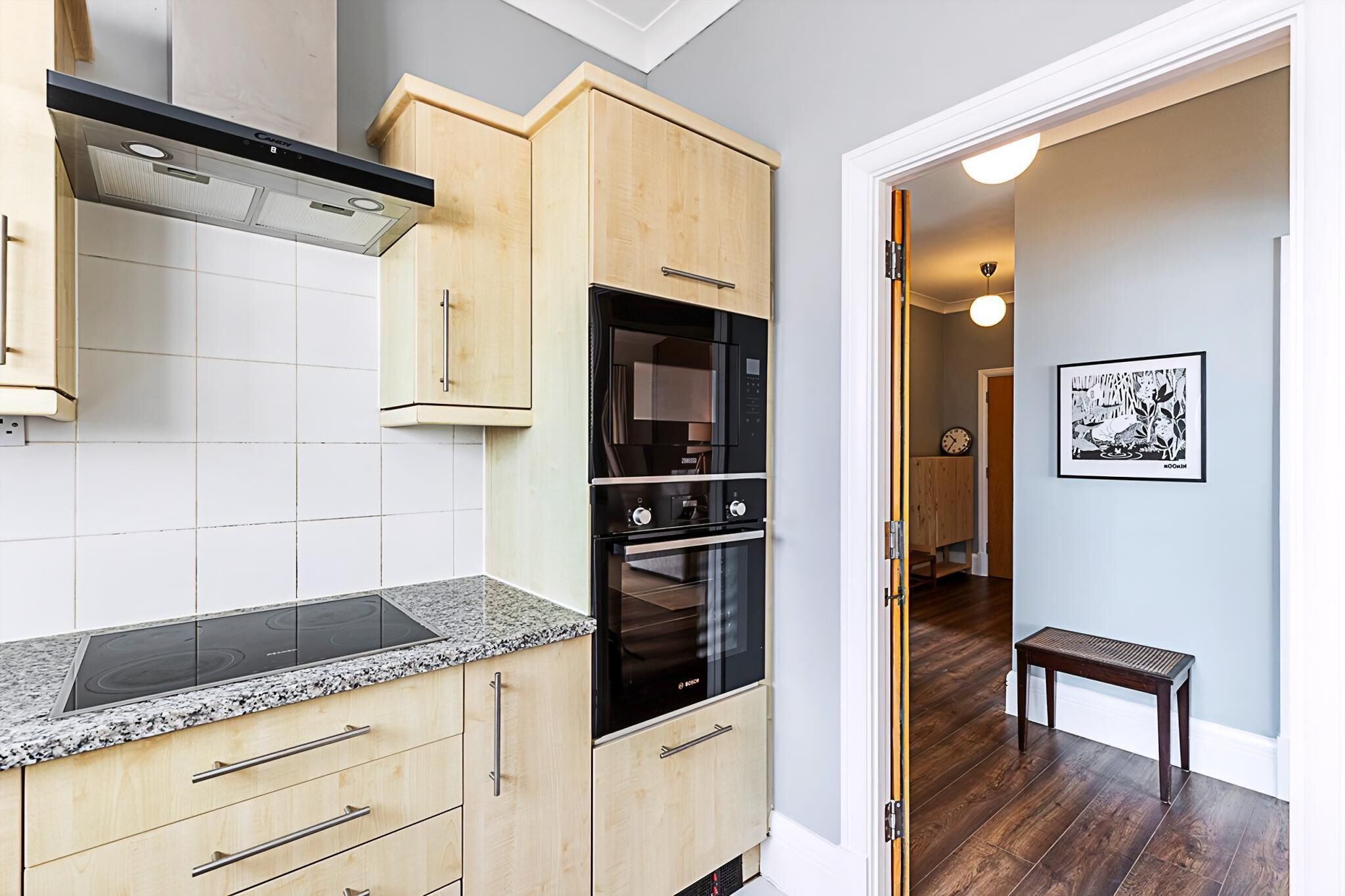 A kitchen with a built-in oven, a stovetop, and wooden cabinets.