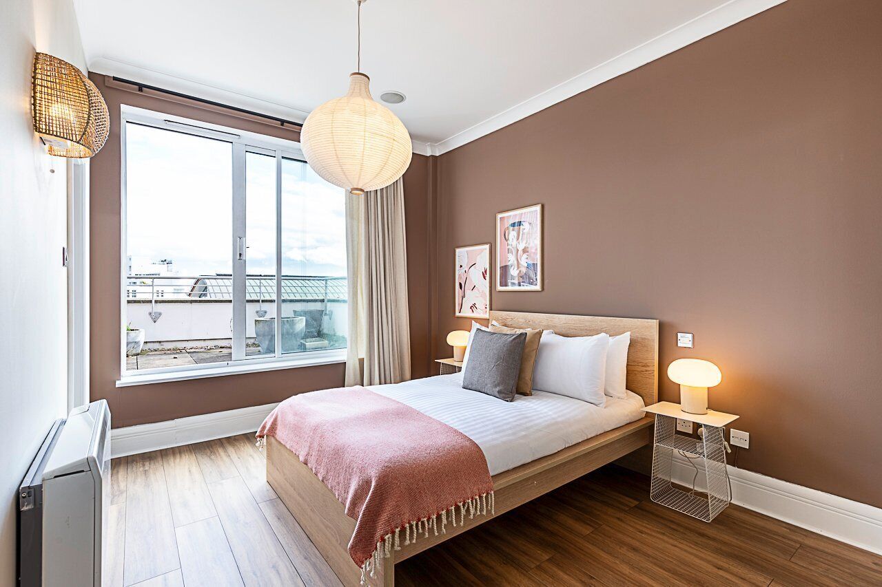 A bedroom with a large bed, bedside lamps, a window with curtains, and a view of the outside.