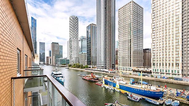 Un immeuble de grande hauteur offrant une vue sur le fleuve, un quai avec des bateaux et un paysage urbain moderne.