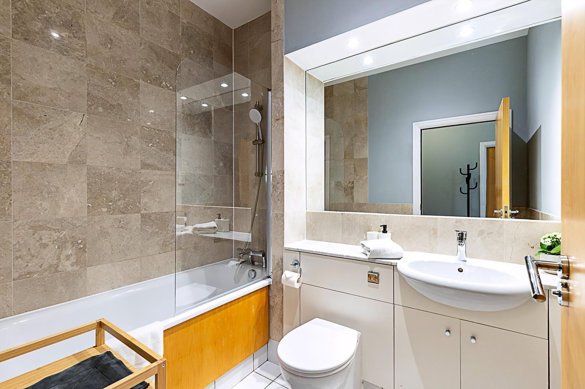 A modern bathroom with a glass-enclosed shower, a white bathtub, a sink, and a toilet.