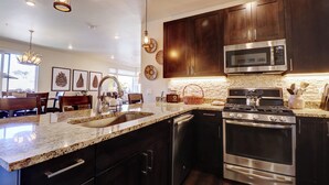 A modern kitchen with dark wood cabinets, stainless steel appliances, granite countertops, and pendant lighting. - Incredible Remodeled Luxury Condo (Dillon)
