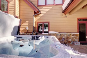 A hot tub in front of a house with a stone wall and a red door.