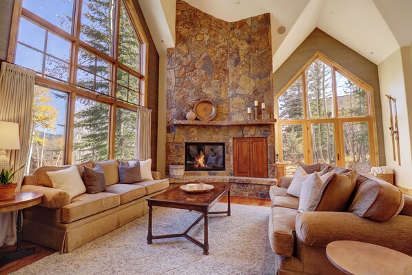 A spacious living room with a stone fireplace, large windows, and a cozy seating area.