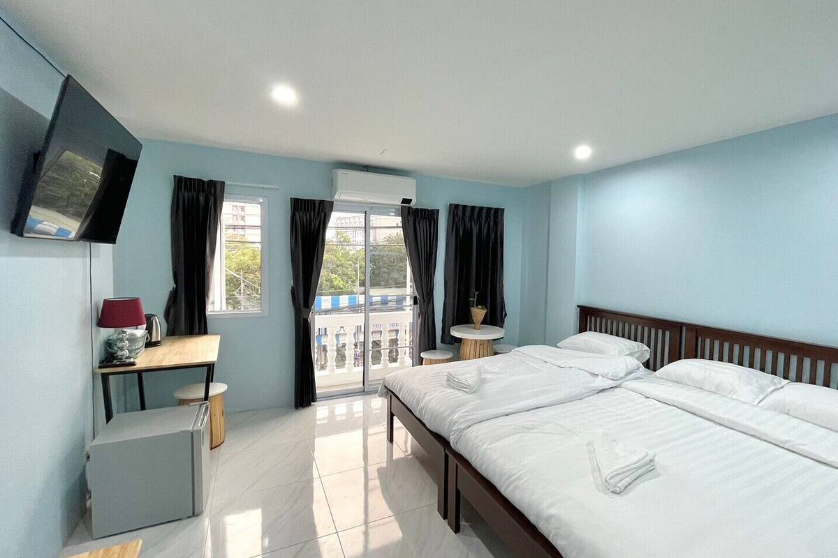 A hotel room with two beds, a TV, a desk with a lamp, and a view of the outside balcony.