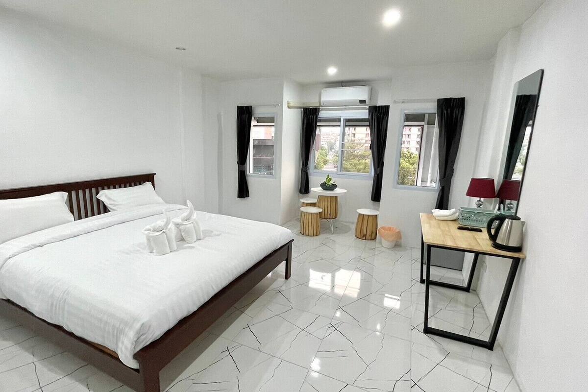 A hotel room with a large bed, a bedside table with a lamp, a small table with a plant, and a mirror on the wall.