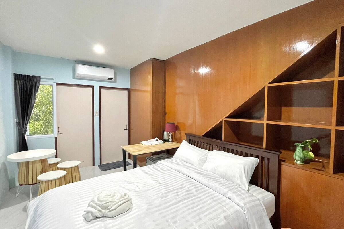 A hotel room with a bed, a desk, a chair, a small table, and a window.