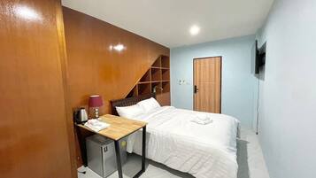 A hotel room with a bed, a desk with a lamp, a small cabinet, and a wardrobe.