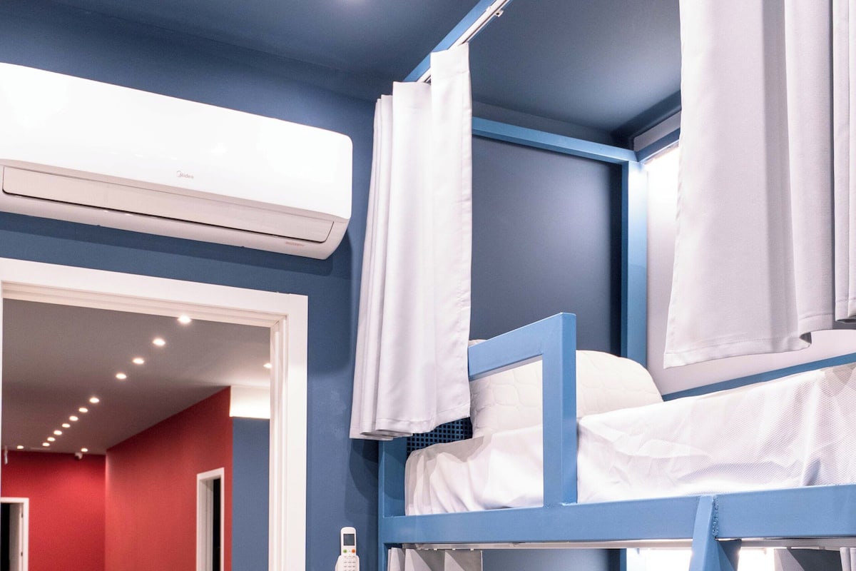 A bunk bed room with a desk and chairs, an air conditioning unit, and a red wall.
