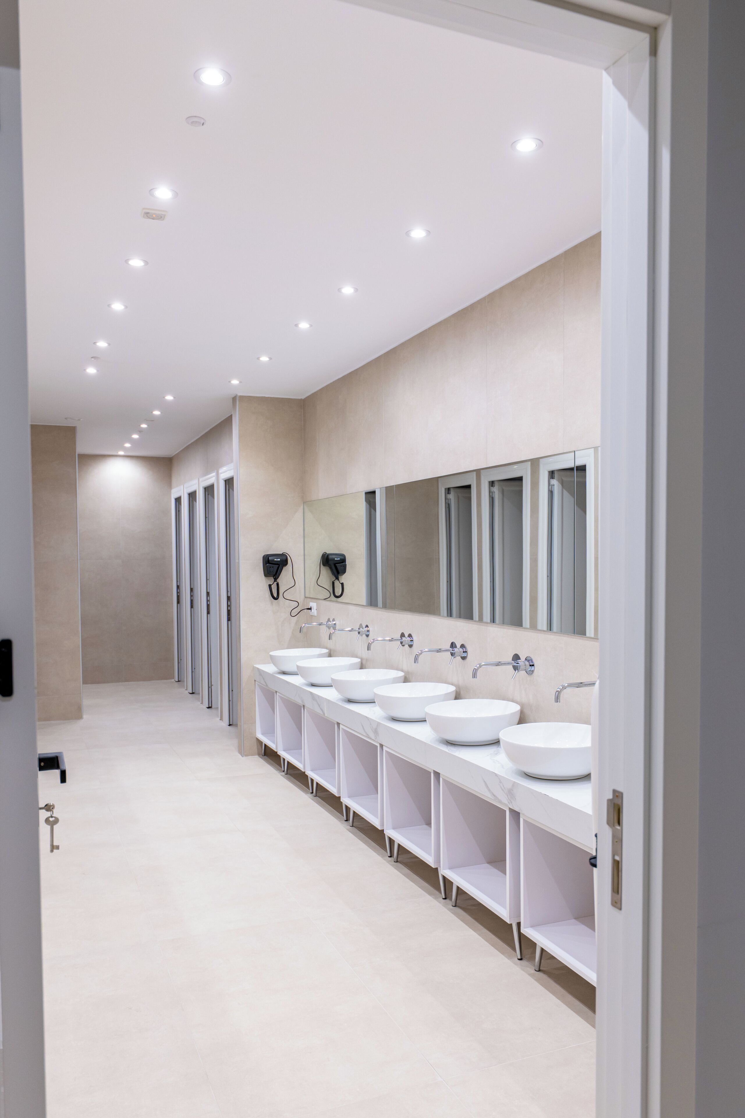 A modern bathroom with multiple sinks, a large mirror, and recessed ceiling lights.
