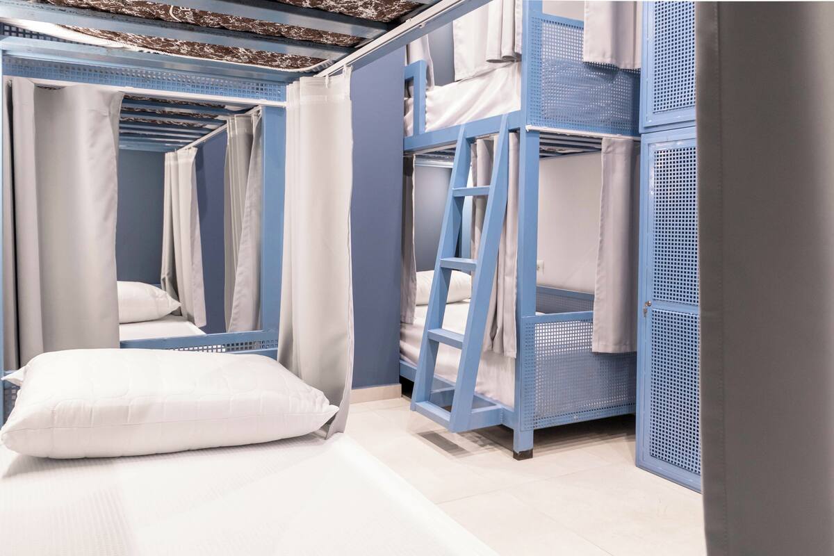 A bunk bed room with a ladder, white bedding, and curtains.