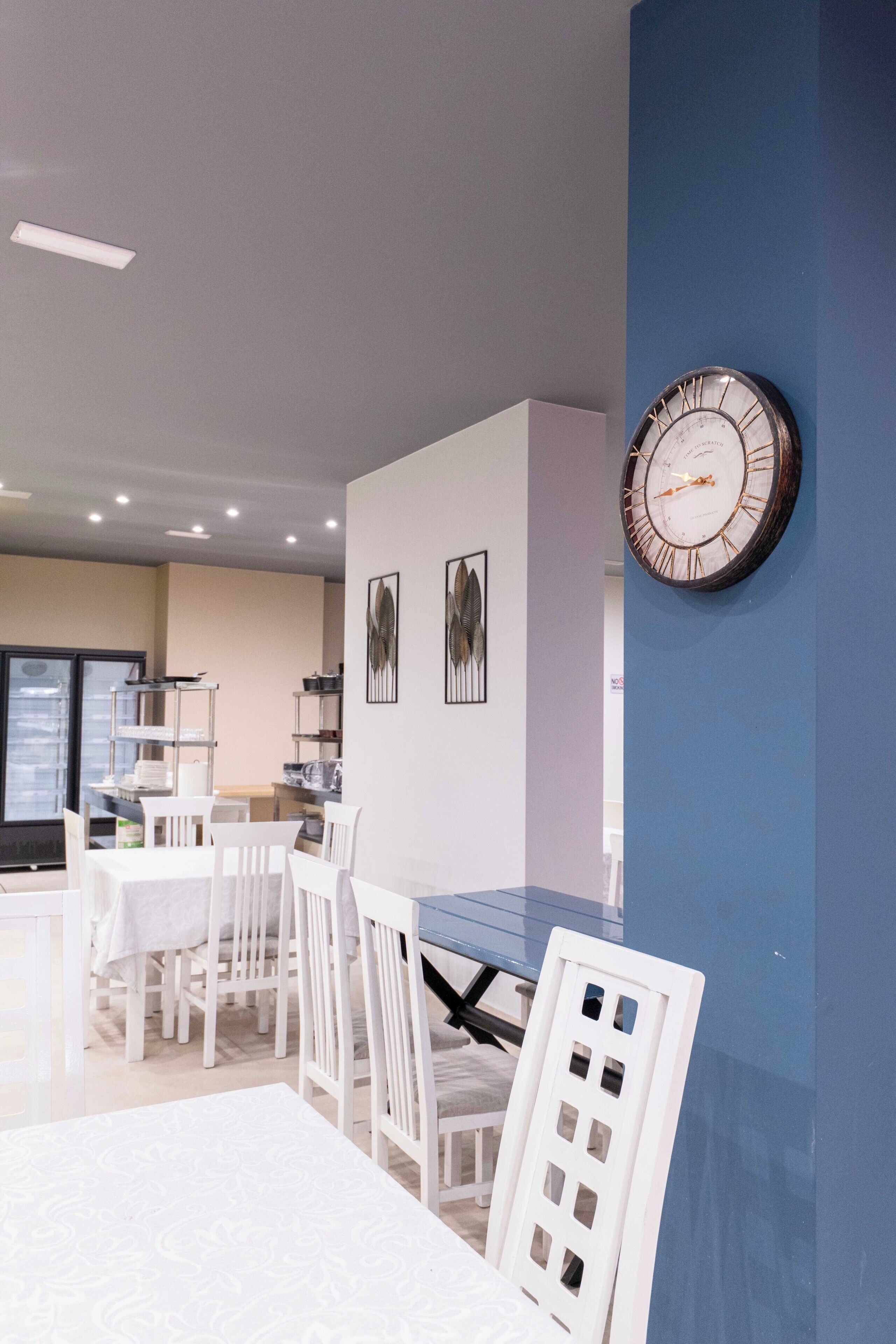 A modern dining area with white furniture, a blue accent wall, and a wall-mounted clock.