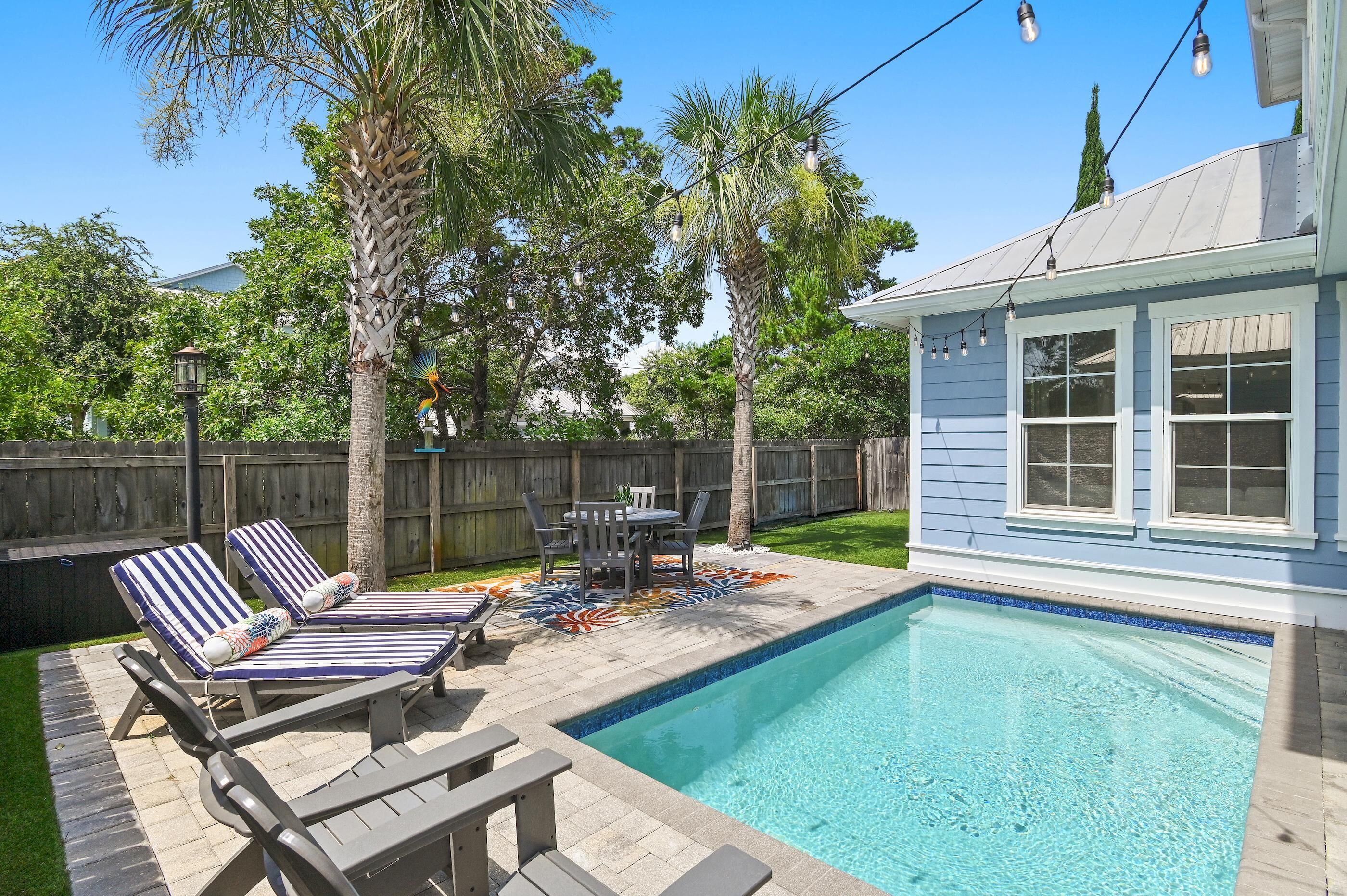 Un jardin avec une piscine, des chaises longues, une table et un tapis décoratif.