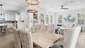 A spacious kitchen with white cabinets, a wooden dining table, wicker chairs, and a chandelier. - Blue Fish Bungalow (Santa Rosa Beach)