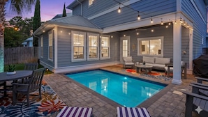 A backyard with a swimming pool, outdoor seating, and string lights. - Blue Fish Bungalow (Santa Rosa Beach)