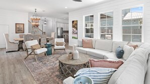 A spacious living room with a white sofa, a dining area with wicker furniture, and a kitchen with white cabinetry. - Blue Fish Bungalow (Santa Rosa Beach)