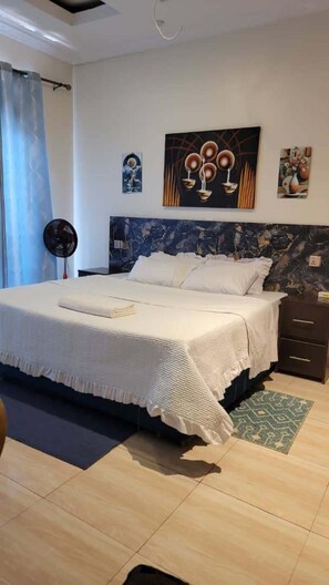 Une chambre à coucher comprenant un lit, une table de chevet, un ventilateur fixé au mur et des œuvres d’art.