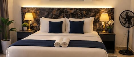 Une chambre d’hôtel avec un grand lit, deux lampes de chevet, un climatiseur fixé au mur et des œuvres d’art au-dessus du lit.