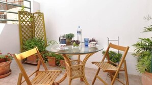 A round glass table with two wooden chairs, surrounded by potted plants and a water bottle. - "The Grey" in Mets (Athina)