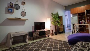 A living room with a TV, a bench, a patterned rug, and a plant. - "The Grey" in Mets (Athina)