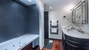 A modern bathroom with a large bathtub, two sinks, and dark tiles.