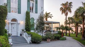 A white building with green shutters, a covered outdoor seating area, and a gravel driveway.