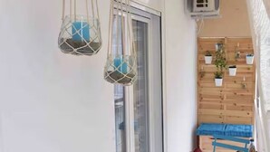 A narrow balcony with a small table, blue folding chairs, and hanging macramé planters. - Glyfada's House Project!
 (Glifada)
