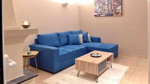 A living room with a blue sofa, a wooden coffee table, a small side table, and a white rug. - Glyfada's House Project!
 (Glifada)