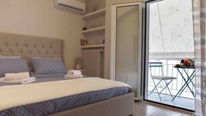 A bedroom with a large bed, a sliding glass door to a balcony, and a small table with fruit. - Glyfada's House Project!
 (Glifada)