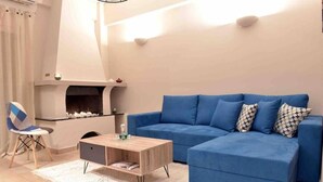 A living room with a blue sofa, a wooden coffee table, a white rug, and a fireplace. - Glyfada's House Project!
 (Glifada)