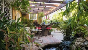 Une terrasse extérieure agrémentée d’une petite cascade, entourée d’une végétation luxuriante et d’une pergola en bois.