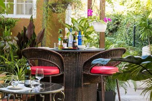 A wicker table with red cushions, surrounded by lush greenery and potted plants. - Serenity Gardens Living (Kingston)