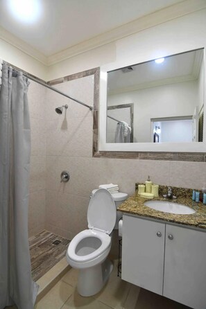 A bathroom with a shower, toilet, sink, and a large mirror. - Serenity Gardens Living (Kingston)