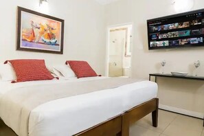 A hotel room with a bed, a painting, a TV, and a small table. - Serenity Gardens Living (Kingston)
