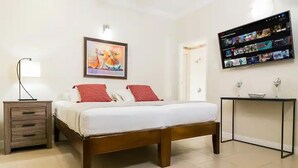 Ein Schlafzimmer mit einem Bett, einem Nachttisch und einem an der Wand befestigten Fernseher, der verschiedene Sender anzeigt.