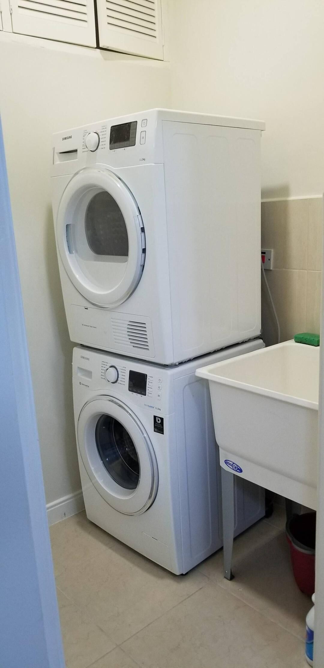 A laundry area with stacked washers and dryers, a white sink, and a green sponge.